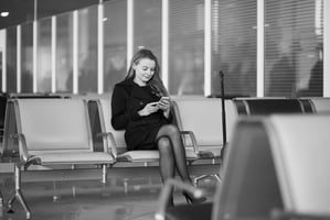 Woman business traveler sitting at airport looking at her phone smiling.
